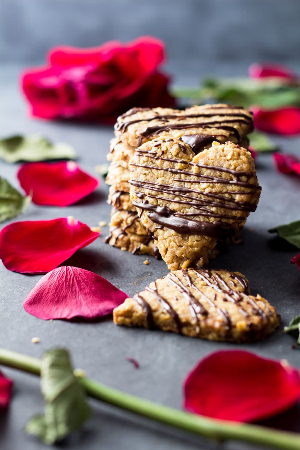 Heart-shaped spelt cookies stacked on the counter with rose petals.