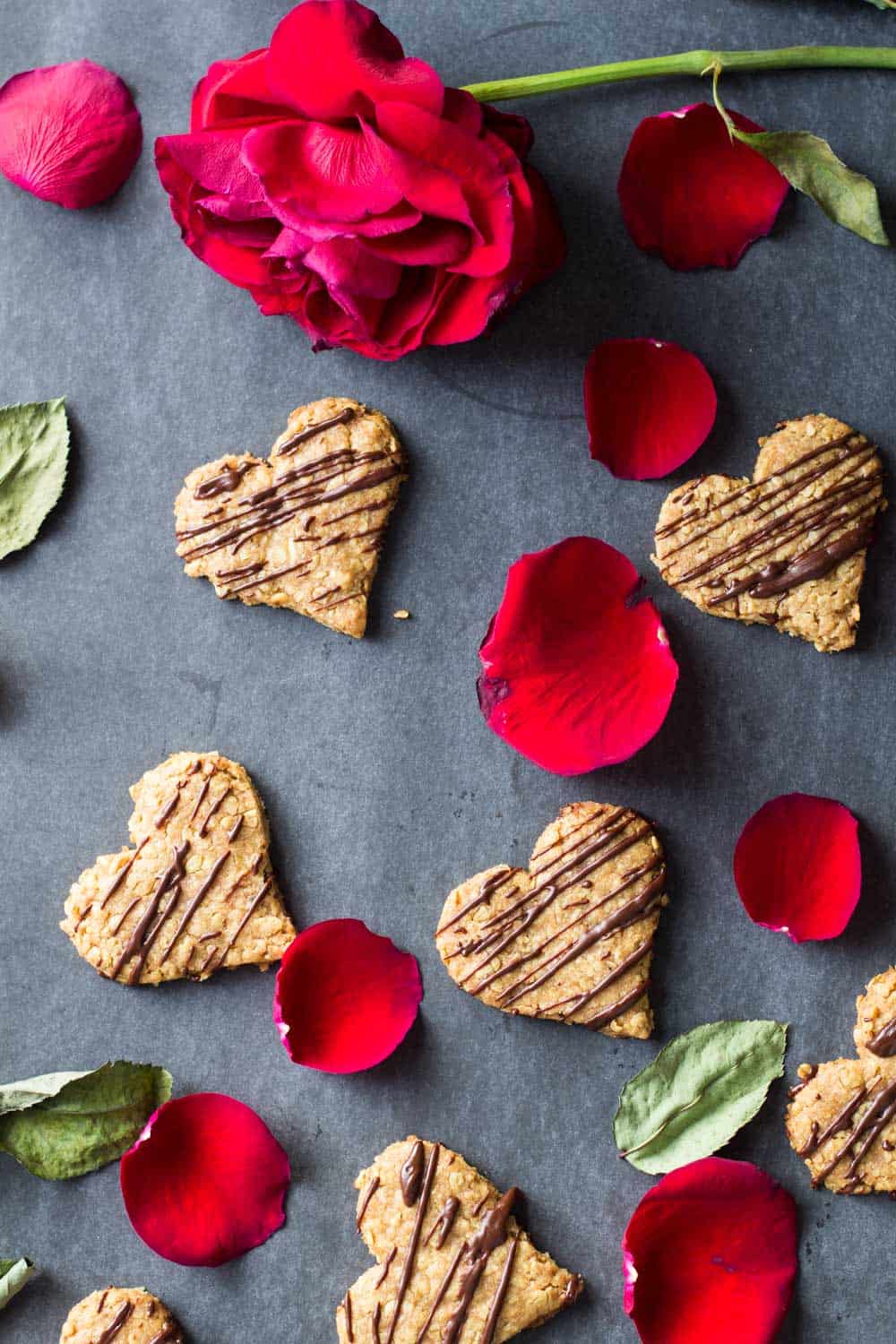 Heart-shaped spelt cookies spread on the counter with a rose and rose petals.