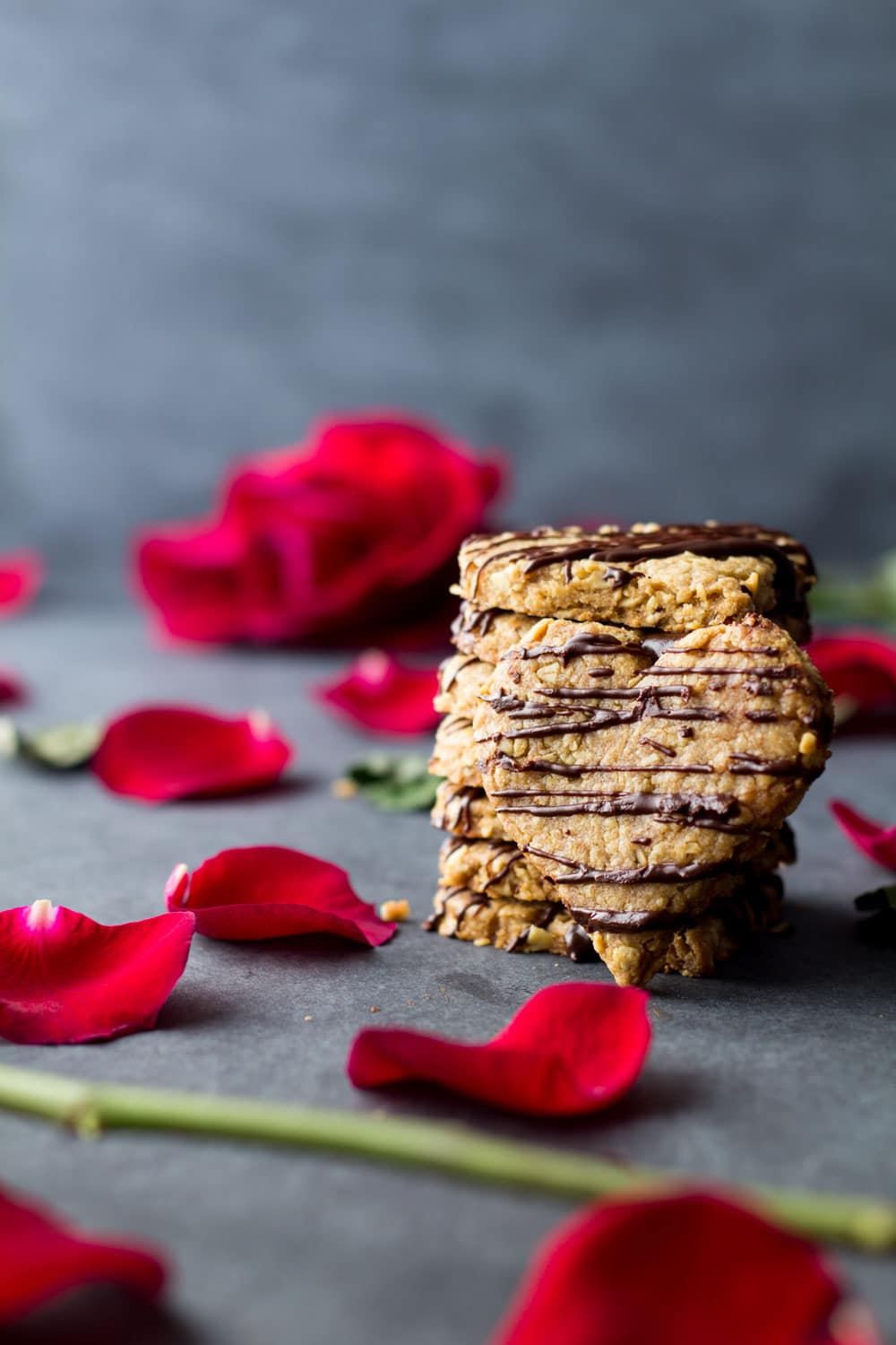 Heart-shaped spelt cookies stacked on the counter with rose petals.