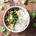 Top view of Peruvian Lamb Stew with rice and peas on a wooden board.