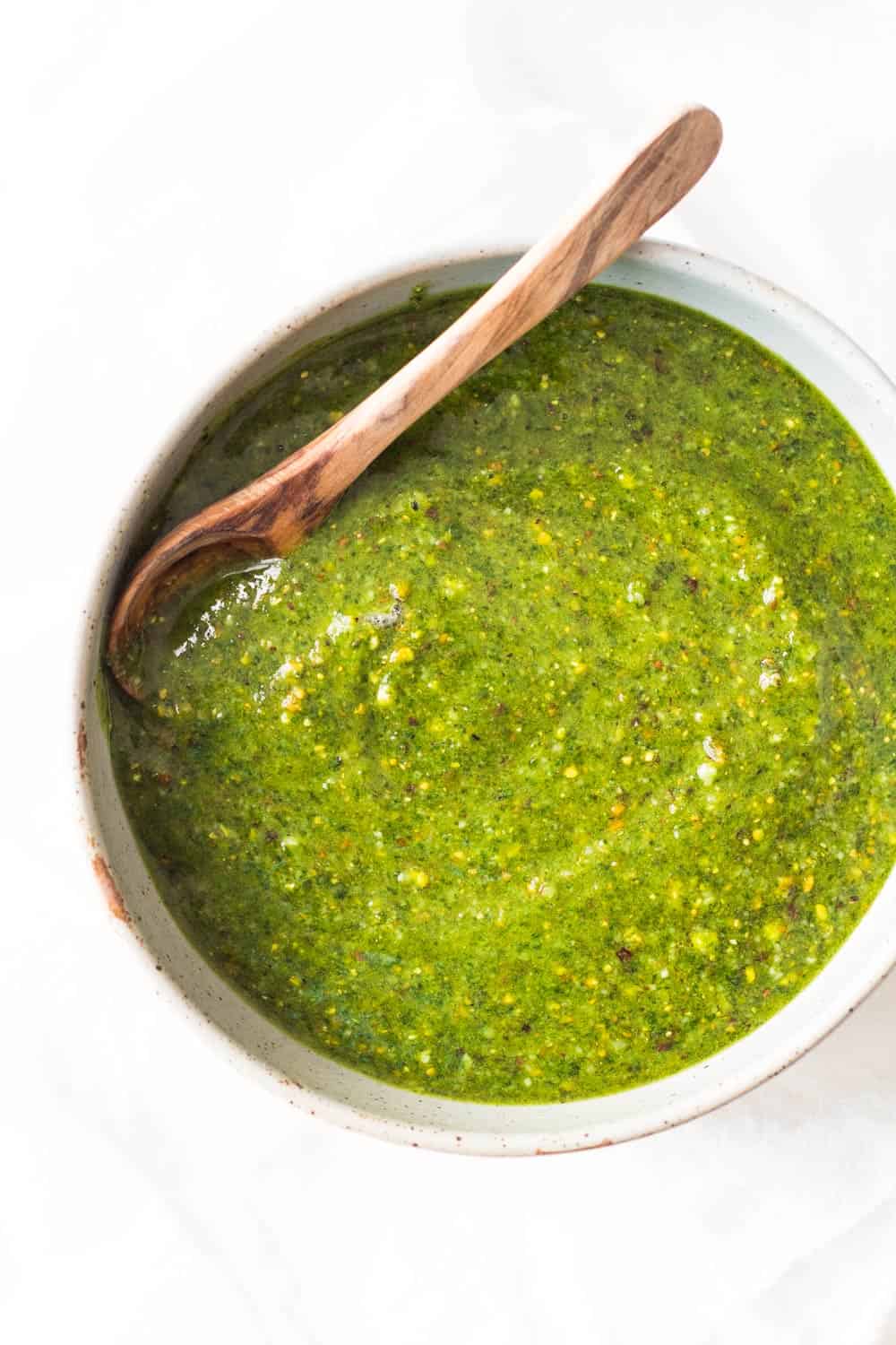 5-Minute Basil Pistachio Pesto in a white bowl with a wooden spoon.