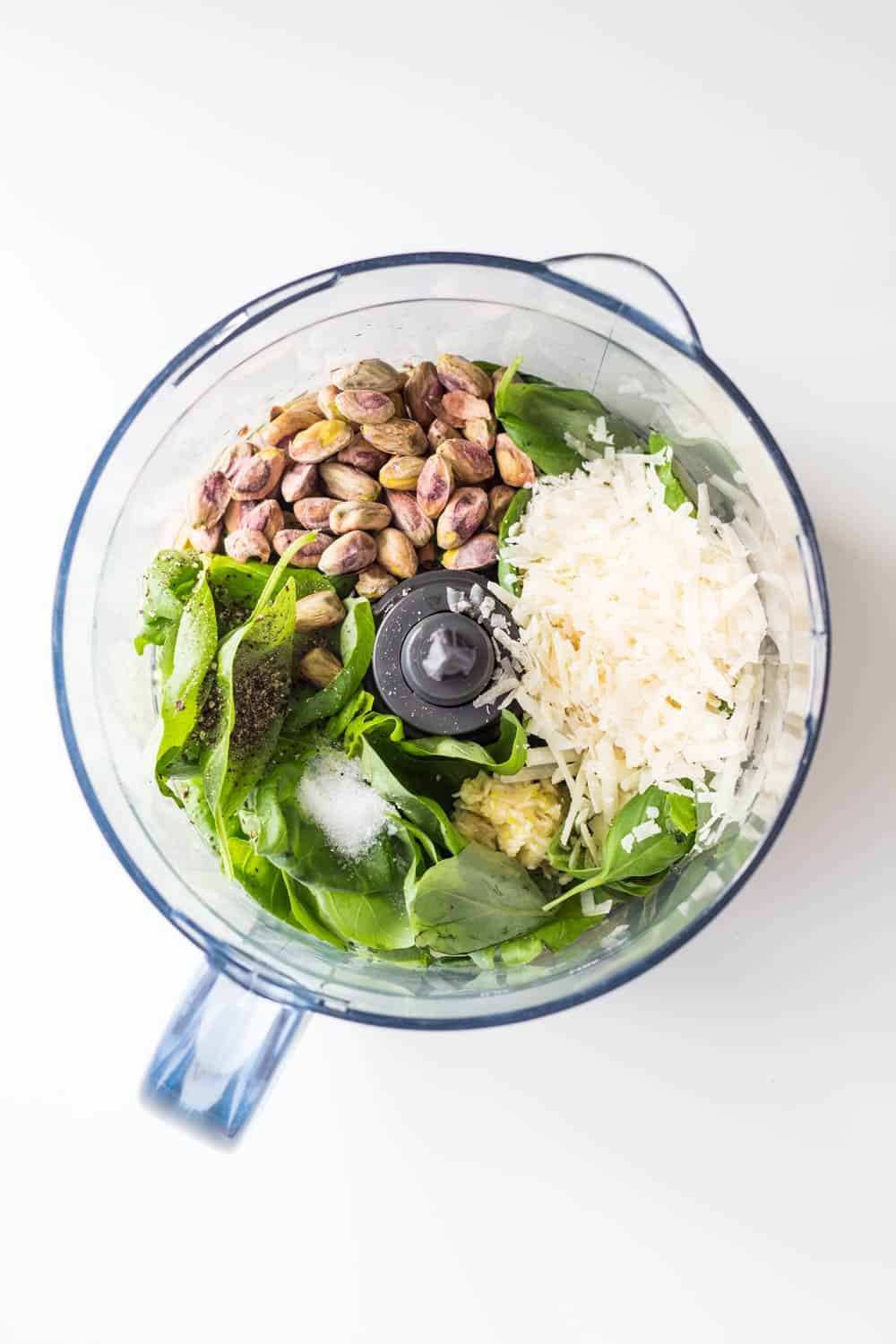 Top view of raw ingredients for 5-Minute Basil Pistachio Pesto in a food processor.