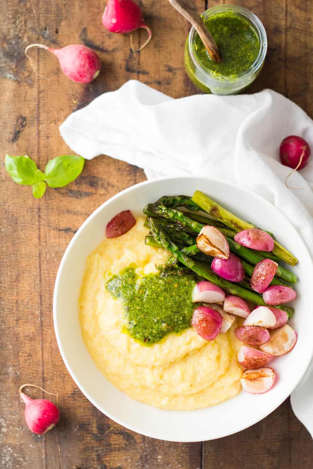 Top view of Creamy Parmesan Polenta with Grilled Vegetables and 5-Minute Basil Pistachio Pesto, an open jar of pesto sauce, and a white napkin.