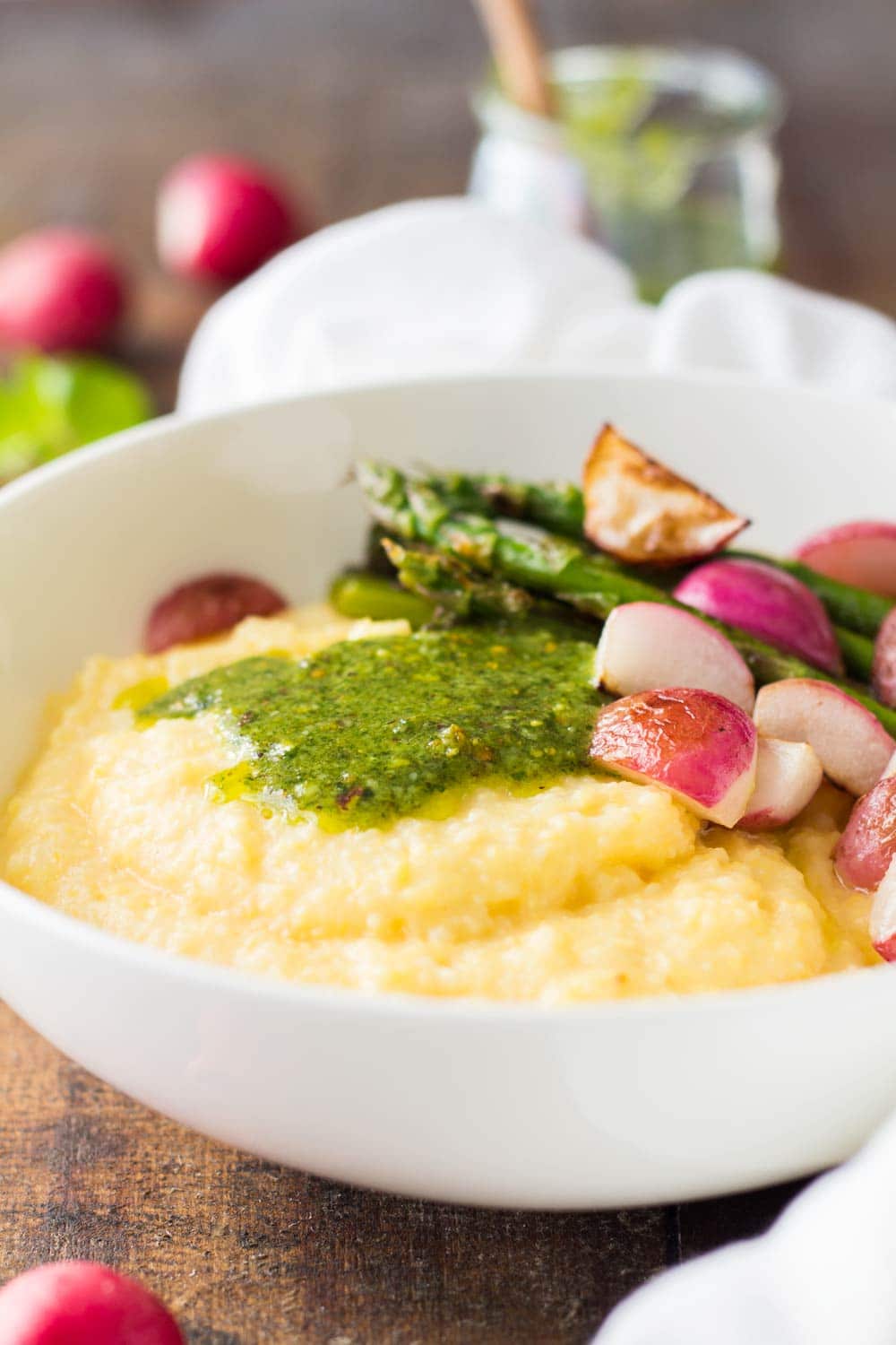 Close up of Creamy Parmesan Polenta with Grilled Vegetables and 5-Minute Basil Pistachio Pesto in a white bowl.