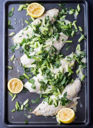 Top view of Snapper Fillet With Celery Parsley Salad on a baking sheet with sliced lemons.