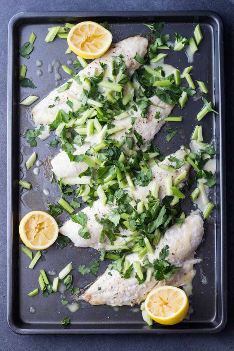 Top view of Snapper Fillet With Celery Parsley Salad on a baking sheet with sliced lemons.