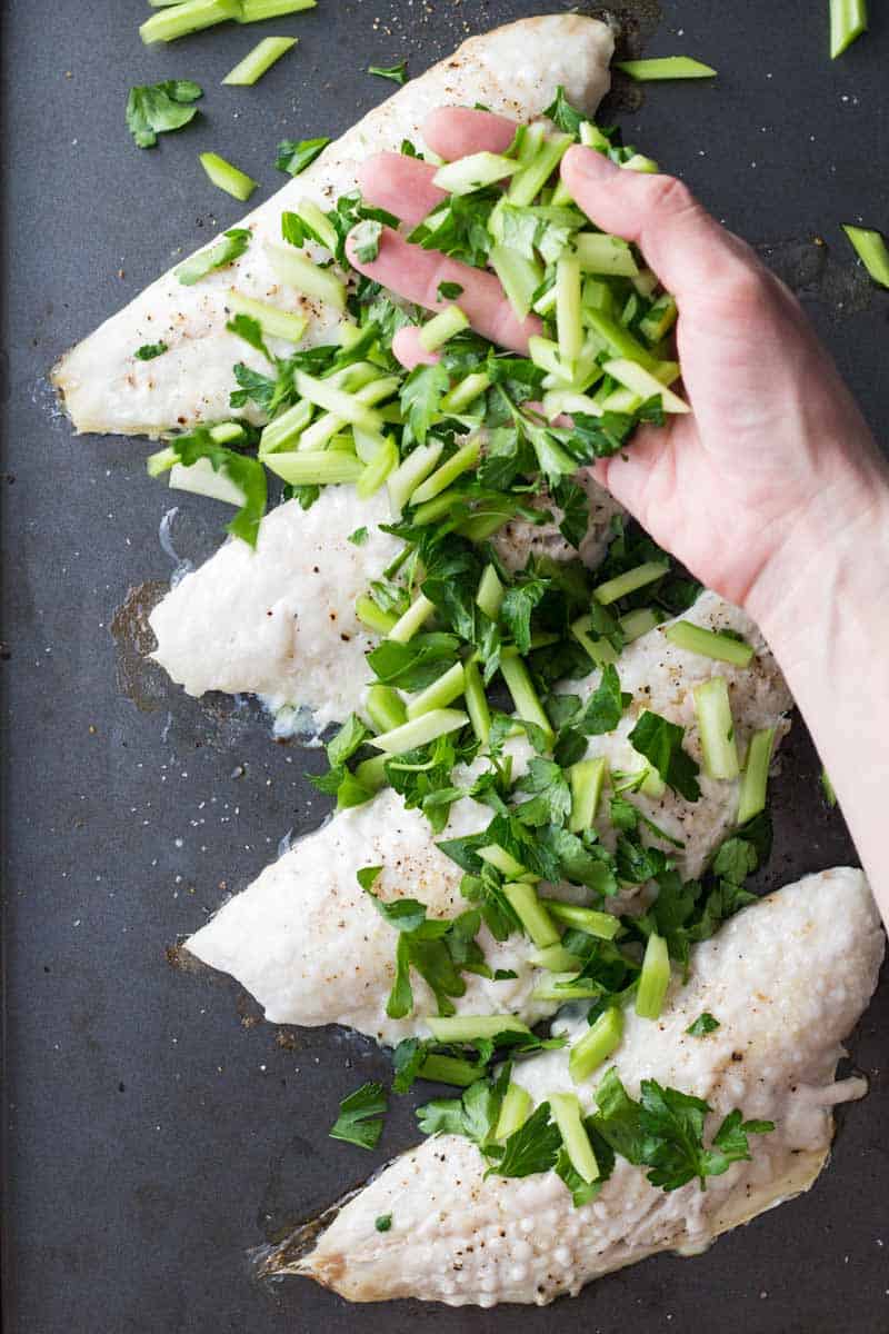 Hand sprinkling chopped celery and parsley over baked snapper filets.