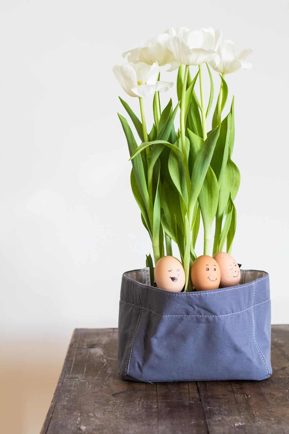 Three Easter Eggs painted with silly faces in a canvas flower pot.