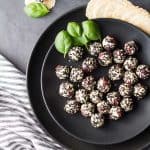 Top view of Easy Goat Cheese Appetizer on a black plate garnished with basil leaves, and a striped napkin.