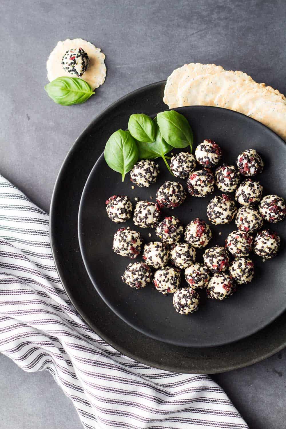 Top view of Easy Goat Cheese Appetizer on a black plate garnished with basil leaves, and a striped napkin.