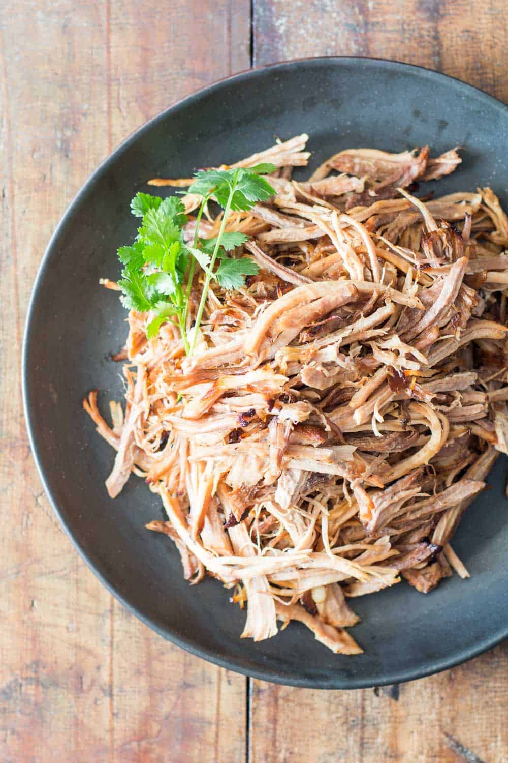 Pulled pork on a black plate garnished with cilantro leaves.