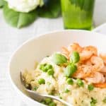 Shrimp and Pea Risotto on a white plate with a fork, a glass of water and a flower.