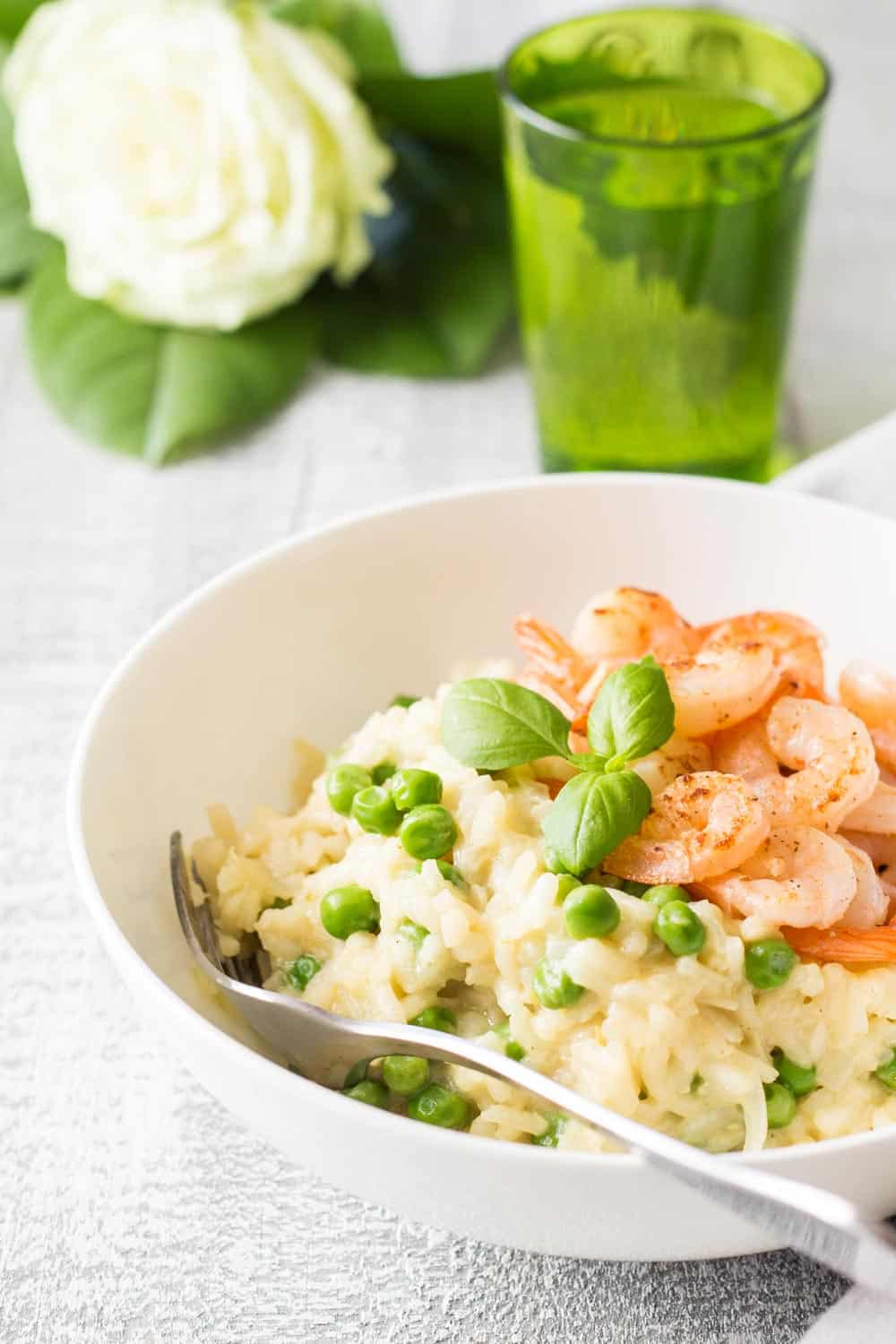 Shrimp and Pea Risotto on a white plate with a fork, a glass of water and a flower.