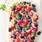 Top view of Summer Fruit Tart garnished with herbs on a rustic board.