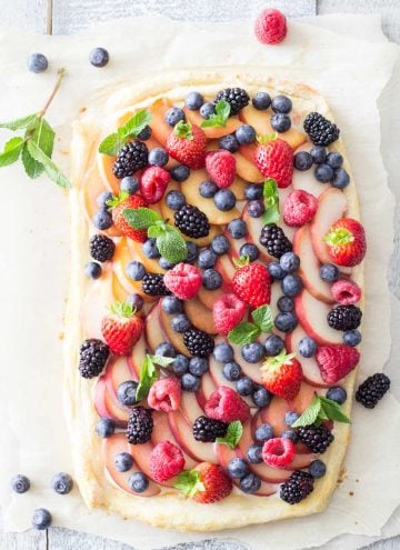 Top view of Summer Fruit Tart garnished with herbs on a rustic board.