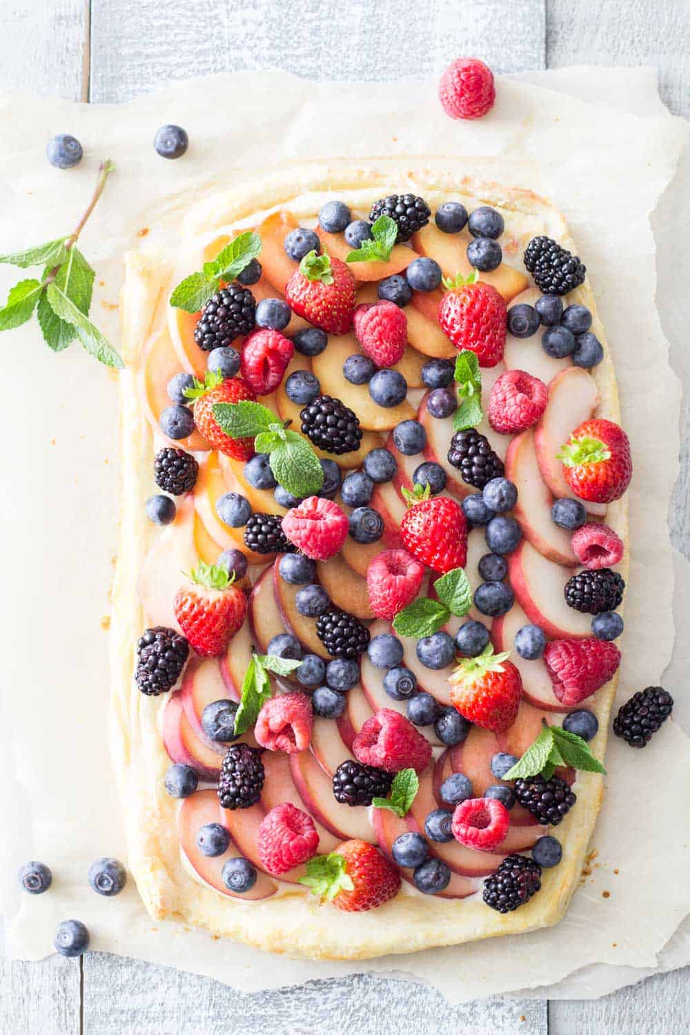 Top view of Summer Fruit Tart garnished with herbs on a rustic board.