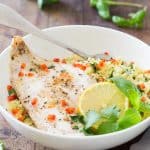 Plate of Baked Haddock with Herb Couscous garnished with fresh herbs, a slice of lemon and a fork.