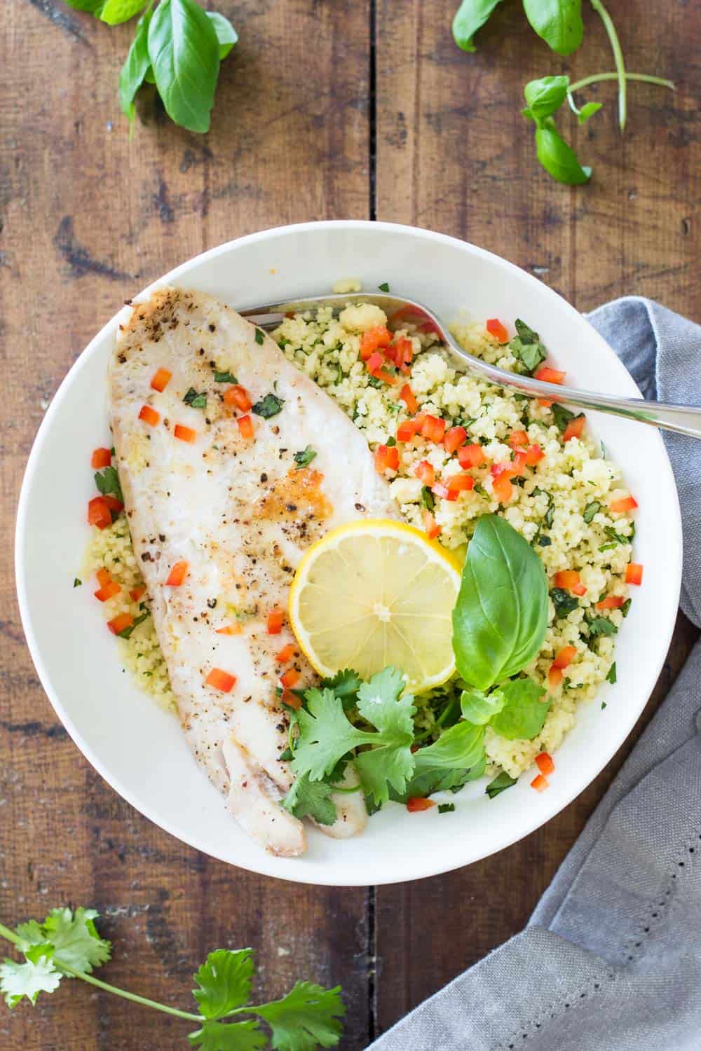 Baked Haddock with Herb Couscous on a white plate with a fork garnished with fresh herbs and sliced lemon.