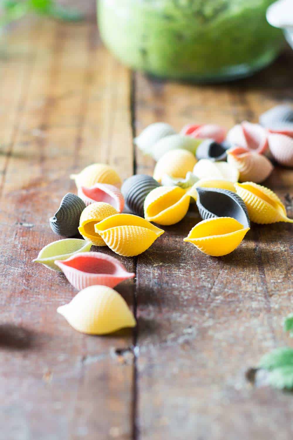 Close up of raw rainbow shell pasta on a rustic wood table.