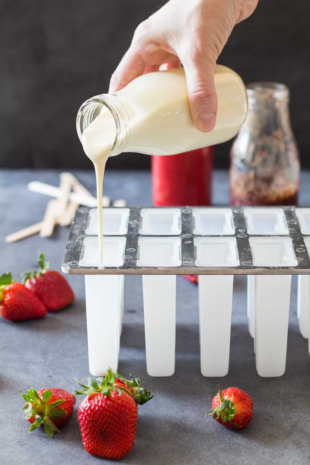 Hand pouring greek yogurt mix into popsicles mold.