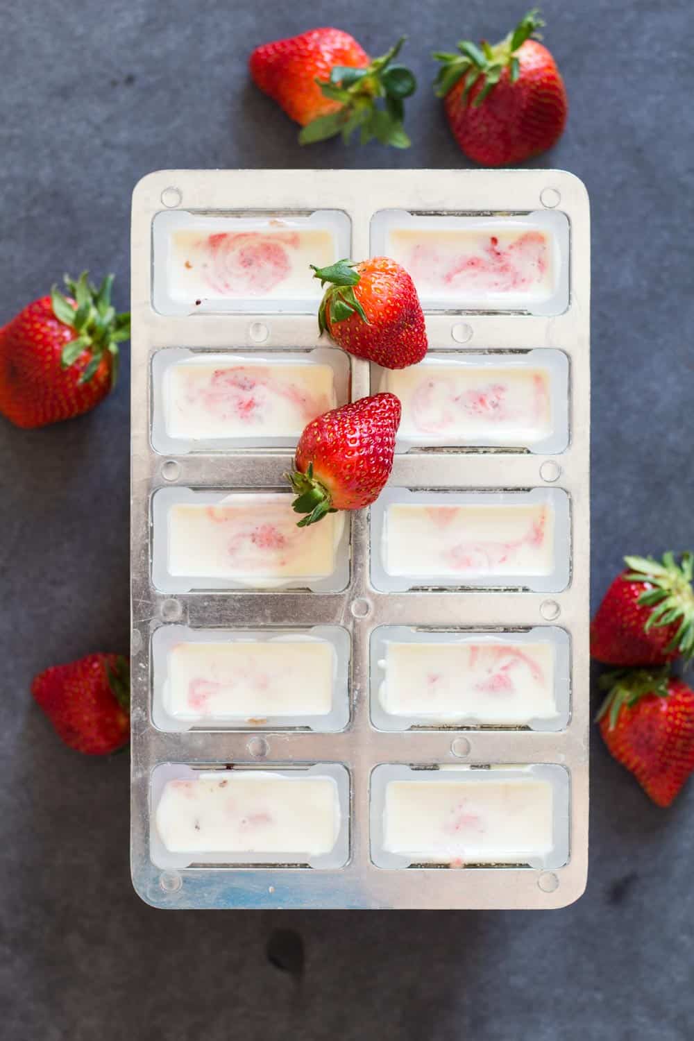 Top view of Greek Yogurt Berry Popsicles in the mold and some fresh strawberries for decoration.