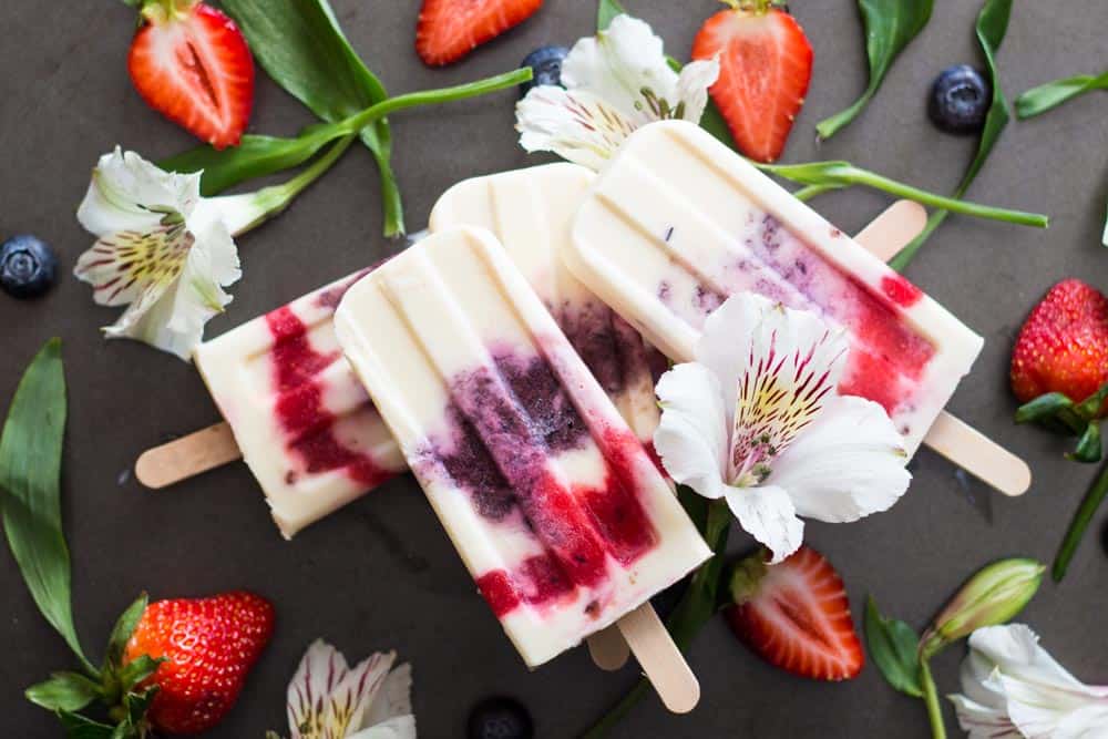 Greek Yogurt Berry Popsicles laid in a pile with fresh flowers and strawberries.