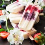 Close up of Greek Yogurt Berry Popsicles laid in a pile with fresh flowers, strawberries and blueberries.