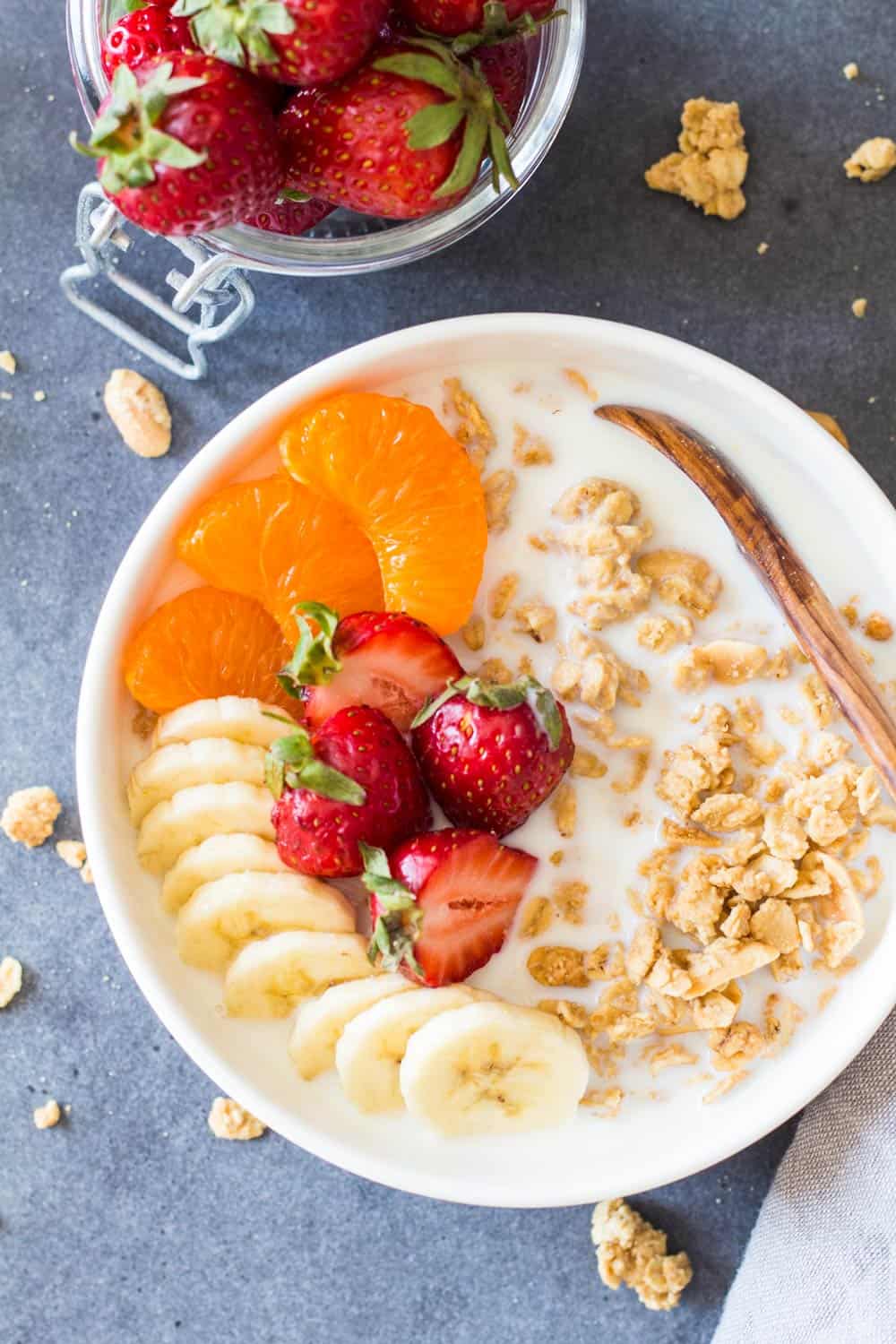 Bowl of Peanut Butter Granola with fruit and milk, and a wooden spoon.