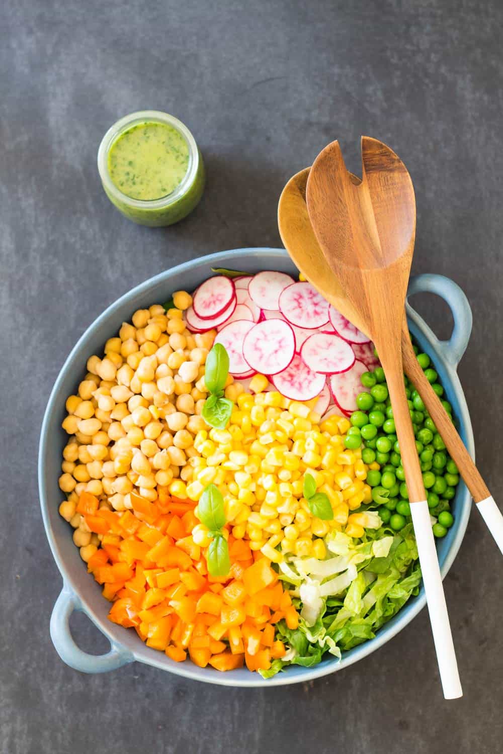 Top view of Romaine Lettuce Salad with a jar of Herb Vinaigrette, and a wooden salad fork and spoon.