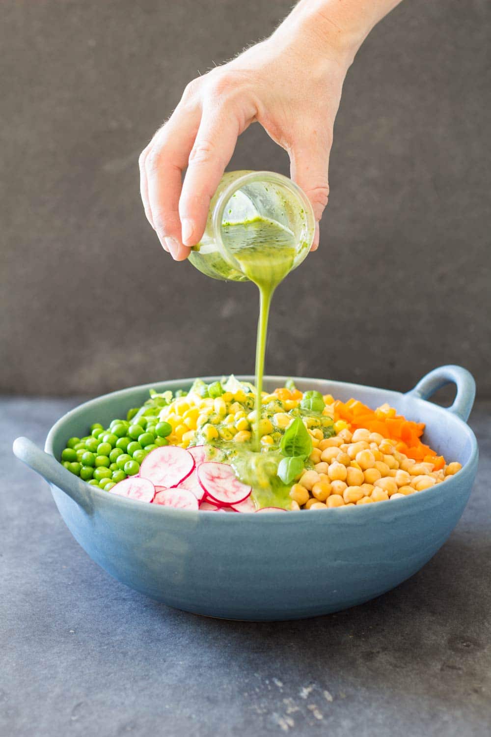 Hand pouring Herb Vinaigrette over Romaine Lettuce Salad in a blue ceramic bowl.