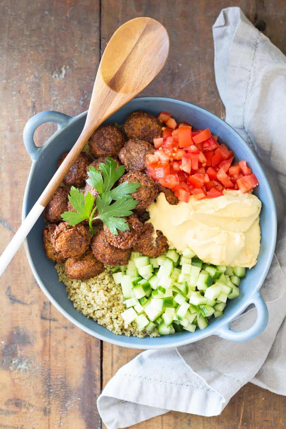 Top view of Vegan Quinoa Falafel Bowl garnished with fresh parsley, and a wooden spoon.