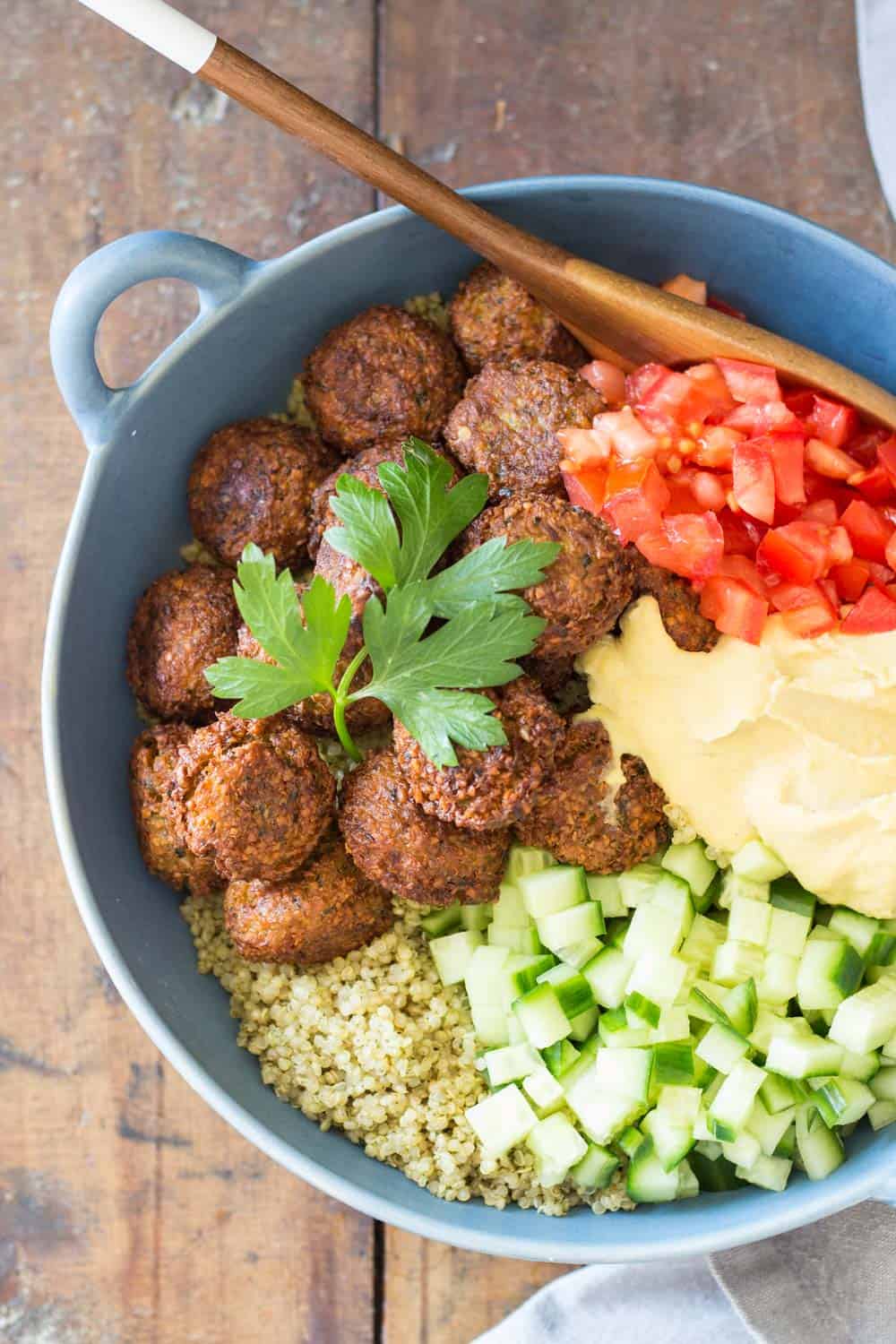 Top view of Vegan Quinoa Falafel Bowl garnished with fresh parsley, and a wooden spoon.