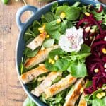 Top view of Watercress Salad with chicken, garnished with a flower, a jar of Basil Clementine Dressing.