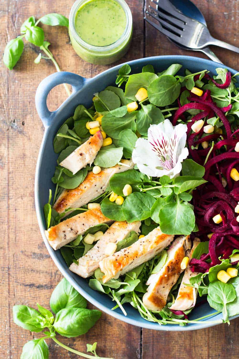 Top view of Watercress Salad with chicken, garnished with a flower, a jar of Basil Clementine Dressing.