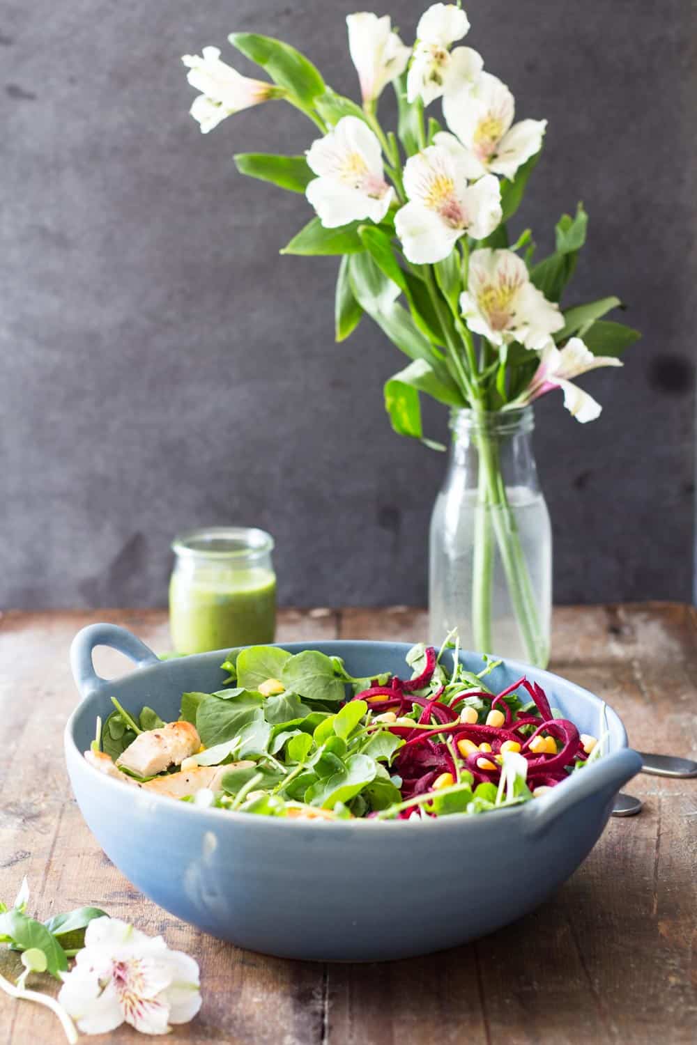 Watercress Salad with Basil Clementine Dressing in a blue bowl, and a vase with flowers.