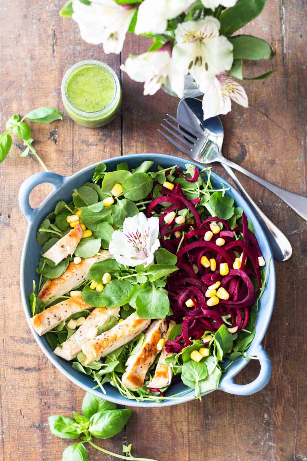 Watercress Salad in a blue bowl, a jar of Basil Clementine Dressing, a fork and a spoon, and flowers.