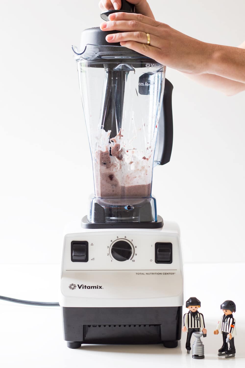 Hands using blender to mix acai. Two toy plastic men standing next to the blender.