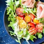 Top view of Arugula Tomato Prosciutto Salad in a blue bowl.