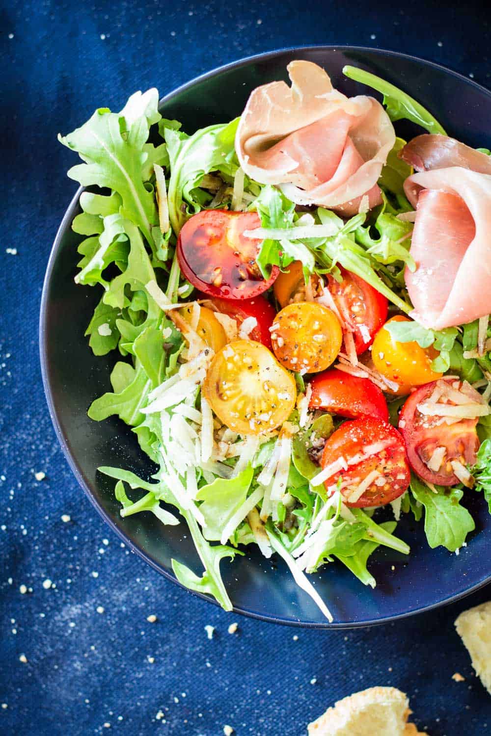 Top view of Arugula Tomato Prosciutto Salad in a blue bowl.