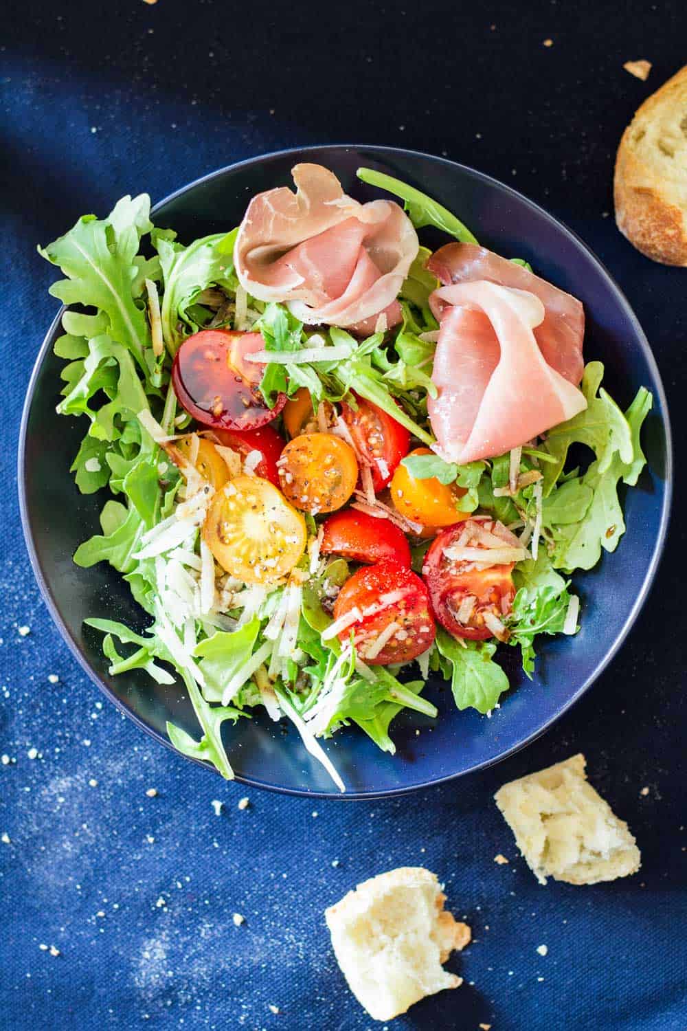 Top view of Arugula Tomato Prosciutto Salad in a blue bowl.