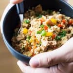 Close up of hands holding a bowl of Cauliflower Fried Rice with a spoon.