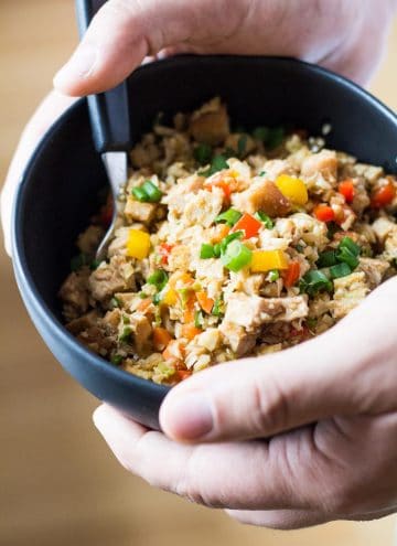 Close up of hands holding a bowl of Cauliflower Fried Rice with a spoon.
