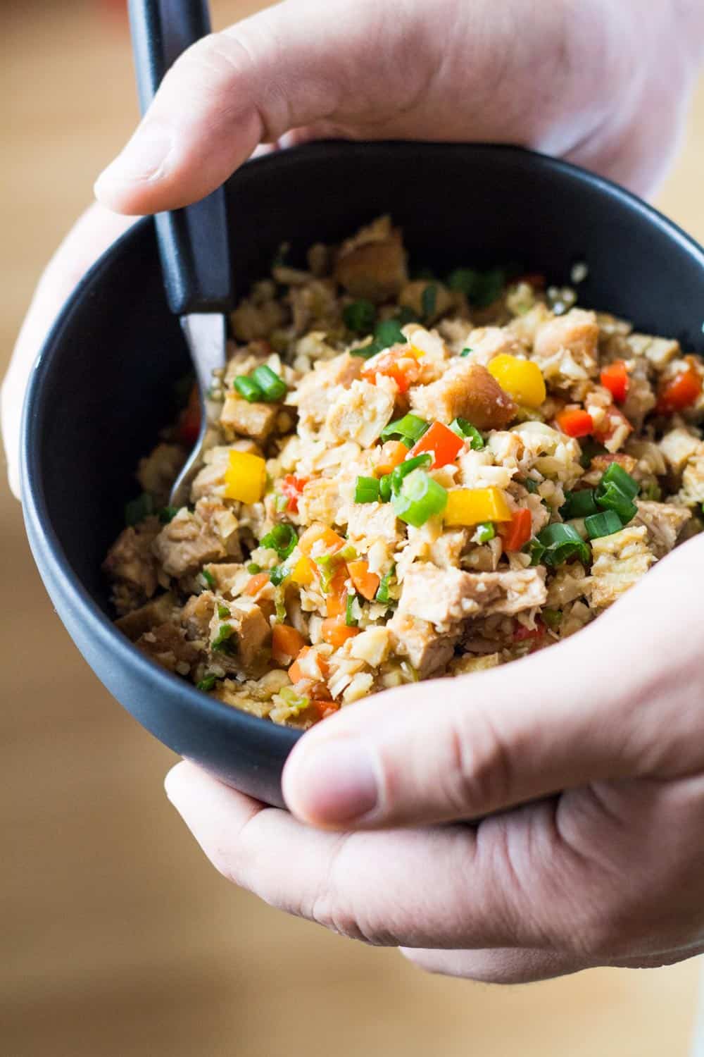 Close up of hands holding a bowl of Cauliflower Fried Rice with a spoon.