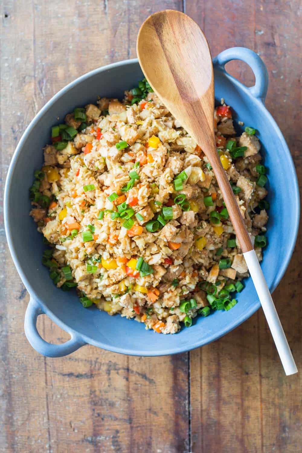 Top view of Cauliflower Fried Rice in a blue bowl with a wooden spoon.