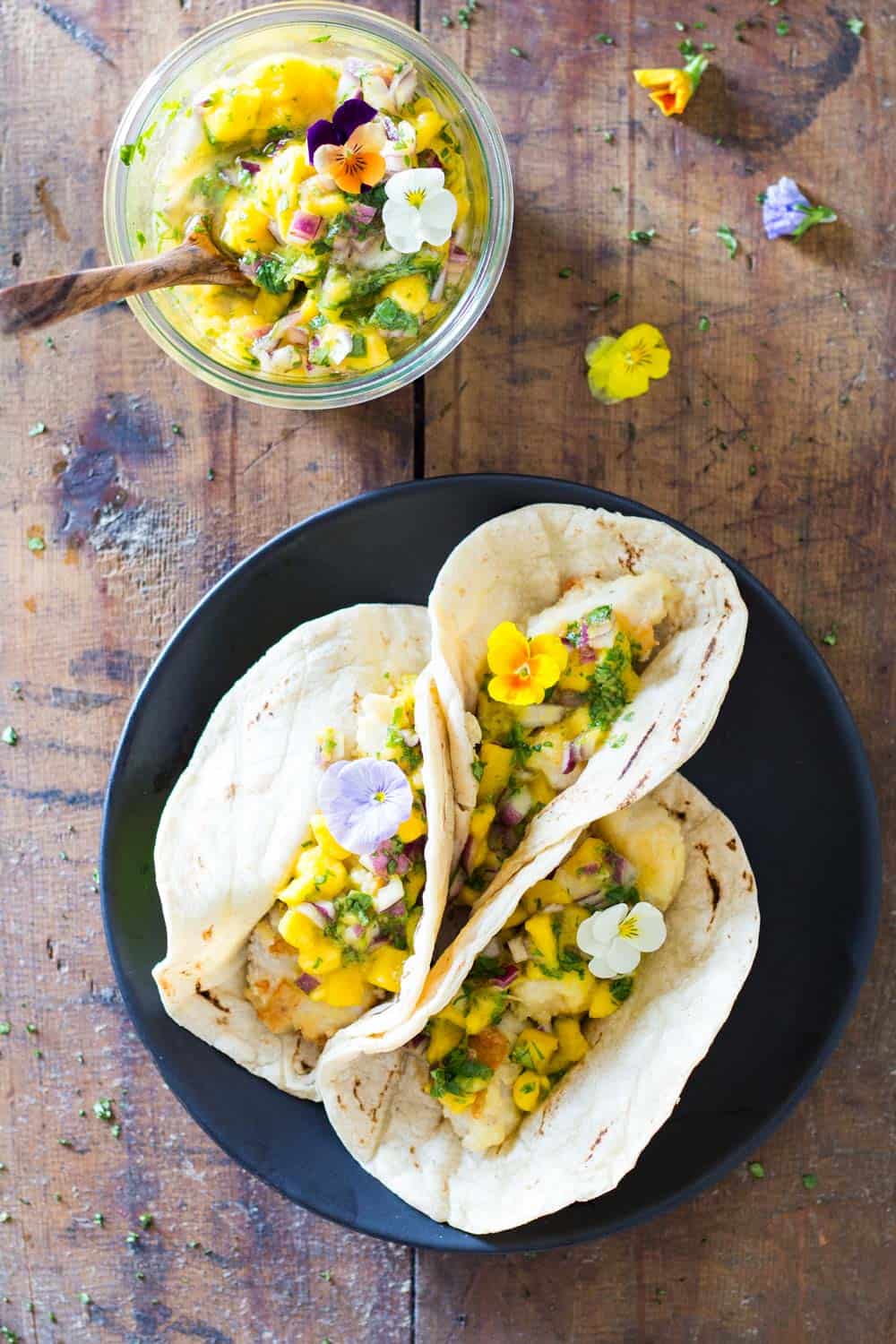 Top view of Easy Fish Tacos on a plate and a jar of Mango Salsa with a wooden spoon.