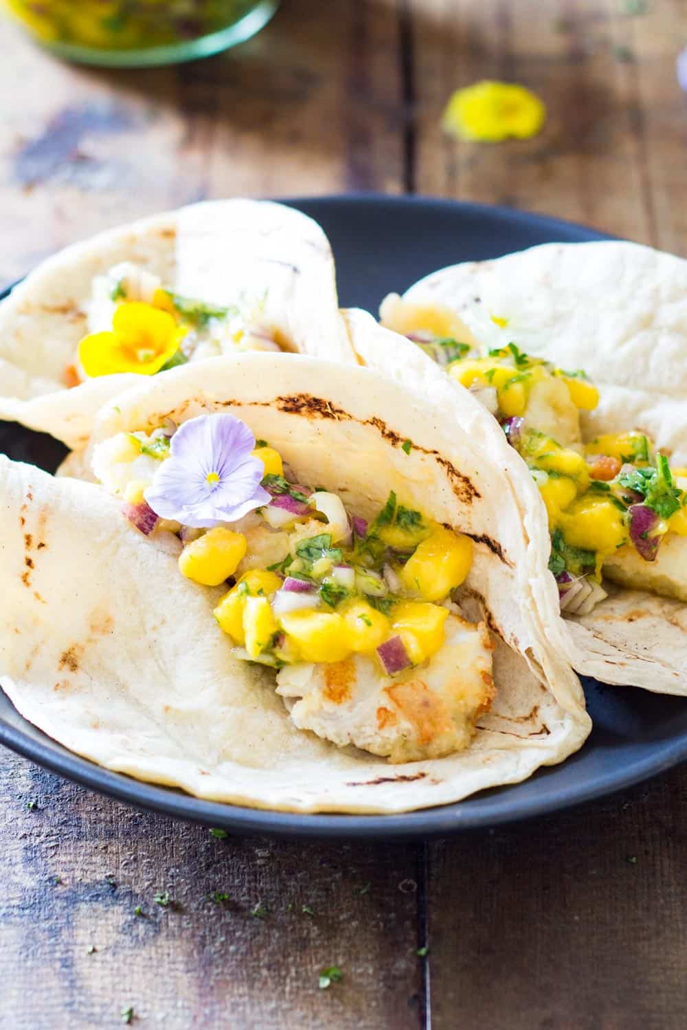 Three Easy Fish Tacos with Mango Salsa on a black plate.