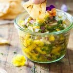 Hand dipping a tortilla chip in a Mango Salsa jar.