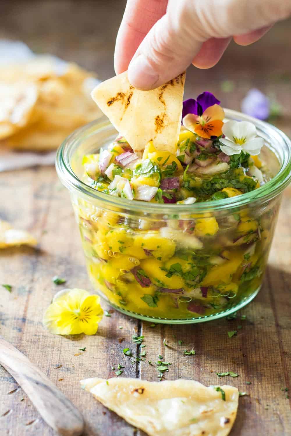 Hand dipping a tortilla chip in a Mango Salsa jar.