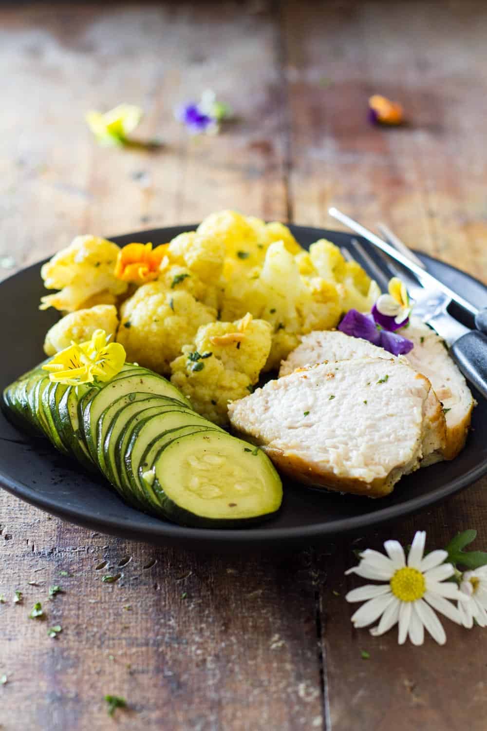 Sliced Curried Chicken with cauliflower and sliced zucchini in a black plate.