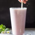 Hand holding a straw in a tall glass of Raspberry Milk.